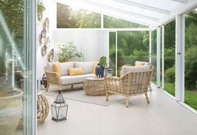 Poppy Sofagruppe in einem Aluminium-Wintergarten von Willab Garden. Gegenlicht scheint hinein und der Hintergrund ist grün und üppig.